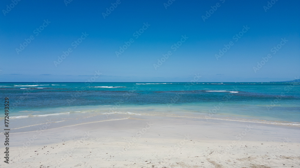Photograph of a beautiful white sand beach. Crystal clear waters with blue tones. Soft waves and green palm trees that give it a tropical touch. Natural landscape. Paradisiac island