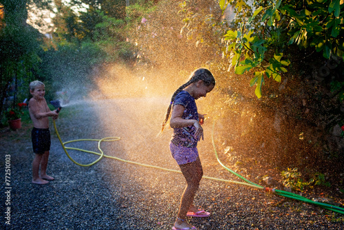 Joyful kids play with water hose in summer light, splashing and laughing in a backyard, creating memories in the golden hour sunlight.