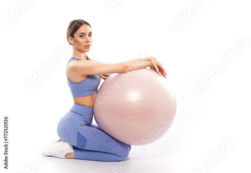 Slim, bodybuilder girl in a lilac tracksuit, sitting on a mat with a Pilates ball,  cardio workout. Sports concept, fat burning and healthy lifestyle.