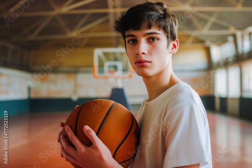 Beautiful Basketball teen male player holding a basket ball posing in basket sports hall.