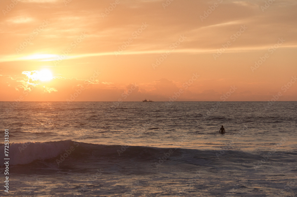 Sunset beach with a surfer on the board, and a cargo boat at the horizon