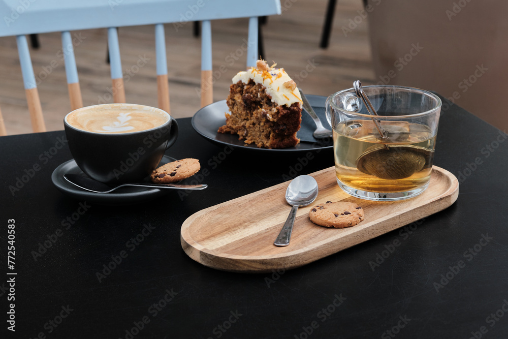 Delicious carrot cake with coffee and cup of tea next to it on wooden table. Cup of cappuccino and tea, slice of carrot pie with walnuts on black table.