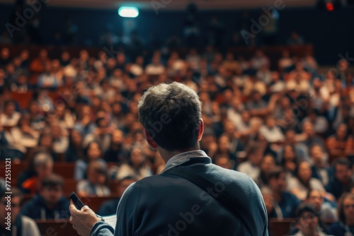 A man stands confidently before a large crowd, passionately delivering a lecture. The audience listens intently, eager to absorb his words of wisdom