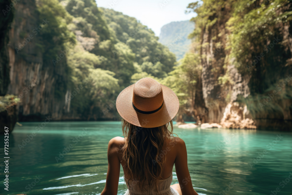 Woman in a straw hat admiring the serene emerald waters surrounded by cliffs.