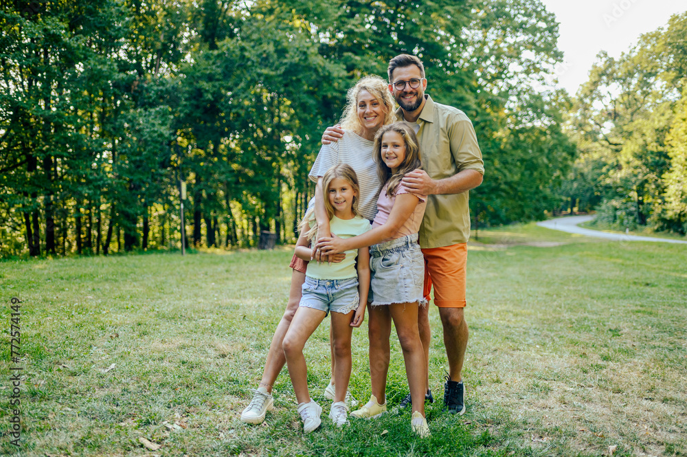 A happy family is standing in nature and hugging while smiling at the camera.