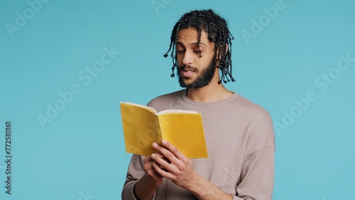 Middle Eastern man reading book from publisher aloud, telling story, enjoying hobby. BIPOC person narrating literature novel, doing critique essay, isolated over studio background, camera B