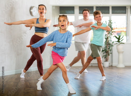 Pleasant little girl engaged in dance in group with her family in light room