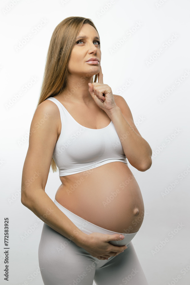Blonde pregnant woman in white clothes looking thoughtful Blonde pregnant woman in white clothes looking thoughtful