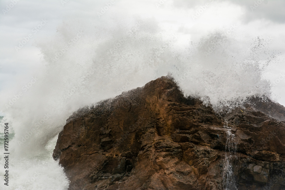 Obraz premium Immense waves hitting a large rock at the edge of the beach. Force of nature.