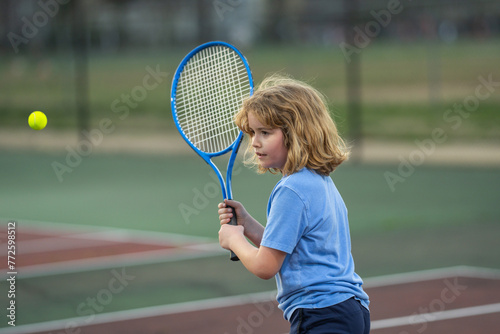 Child playing tennis on outdoor court. Child with tennis ball. Sport child with racket on tennis playground during training in summer.