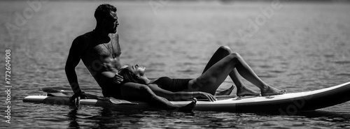 Summer love. Sexy couple rest on paddle board. Sexy woman and man rest on paddleboard in water. Healthy summer lifestyle. Sexy couples. Hot summer. Summer rest. Black and white photo.
