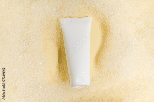 White mockup tube of cream or lotion in water with foam on yellow isolated background. The concept of beauty care and moisturizer cosmetics for the face.