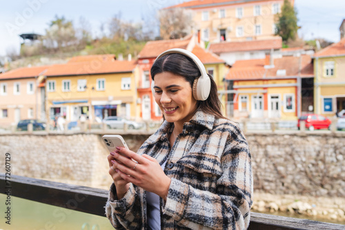 One young girl is listening to music on her wireless headphones and using her phone outdoors on a sunny day 