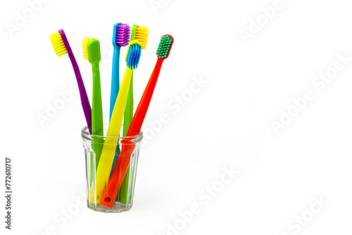 Three toothbrushes - purple, orange and yellow with different colored bristles in a clear cup on a white background. Insulated. Vertical. Photo in high quality.