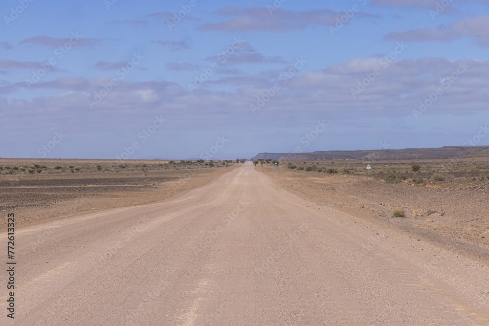 Panoramic picture over a gravel road through the desert like steppe in southern Namibia under a blue sky