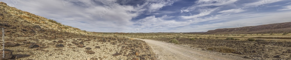 Panoramic picture over a gravel road through the desert like steppe in southern Namibia under a blue sky