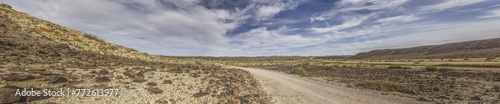 Panoramic picture over a gravel road through the desert like steppe in southern Namibia under a blue sky