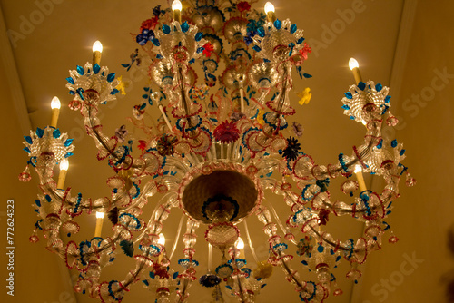 Opulent Murano glass chandelier adorned with colorful floral accents, creating a luxurious atmosphere with its lit candles and intricate glasswork