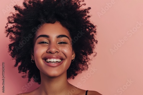 Portrait of a beautiful young african american woman with afro hairstyle smiling against pink background