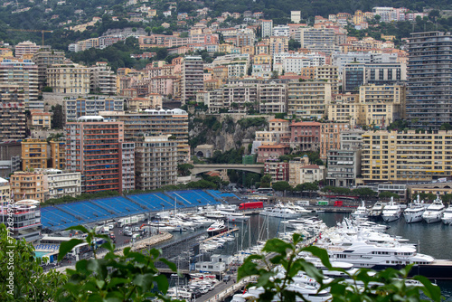 The Monte Carlo waterfront is alive with a cluster of luxury yachts juxtaposed against the colorful, urban architecture of the city's dense skyline
