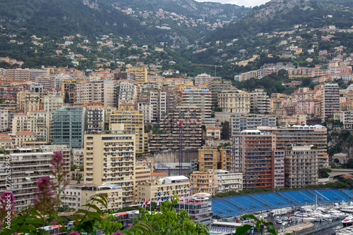 Overlooking the Monte Carlo marina, this image captures a collage of modern and traditional buildings amid lush hills, with yachts docked below