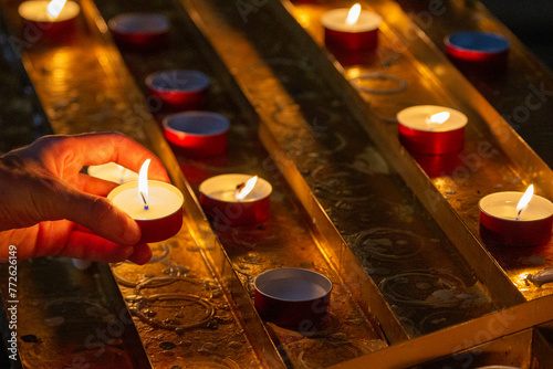 A hand gently places a lit candle among others in a peaceful act of remembrance, the warm glow symbolizing hope and memory