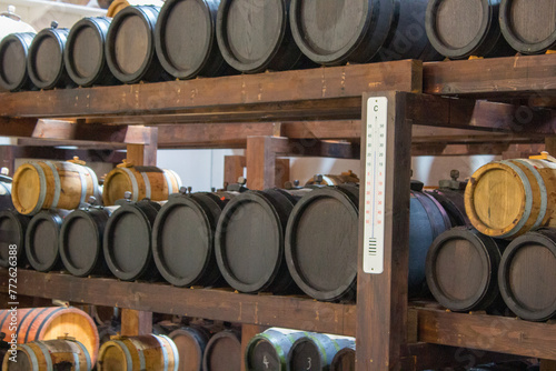 Wooden barrels of varying sizes are methodically stacked on shelves in a cellar, possibly containing wine or spirits, ready for the aging process