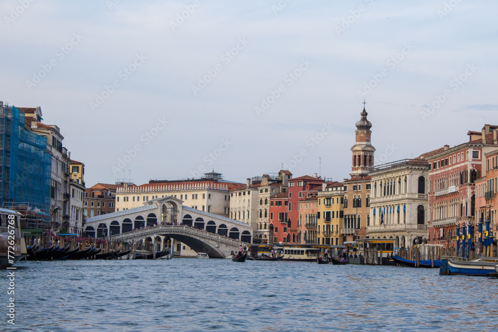 The Rialto Bridge stands proudly over the Grand Canal in Venice, framed by historic facades, under the watchful eye of a campanile in the distance.