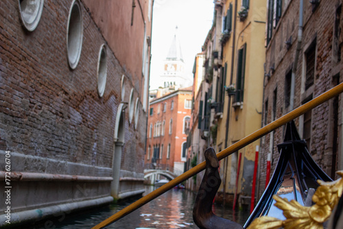 The intimate perspective from a gondola navigating a narrow, secluded canal in Venice, edged by the textured walls of ancient buildings.