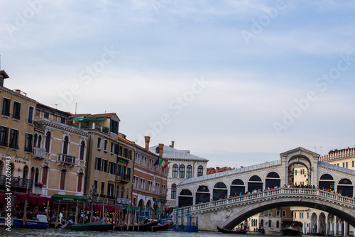 The iconic Rialto Bridge stretches over Venice's Grand Canal against a backdrop of historic buildings and vibrant street life, a testament to Venetian heritage.