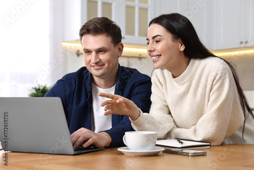 Happy couple using laptop together at wooden table in kitchen