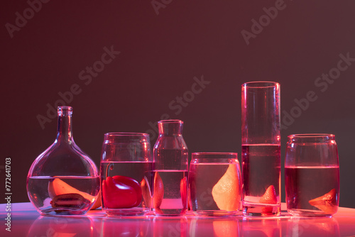 fruits and vegetables are behind the vessels with water on a pink-blue background at studio
