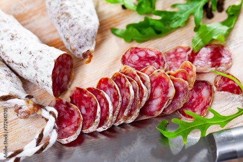 Sliced Catalan sausage Fuet on wooden table with arugula and black pepper