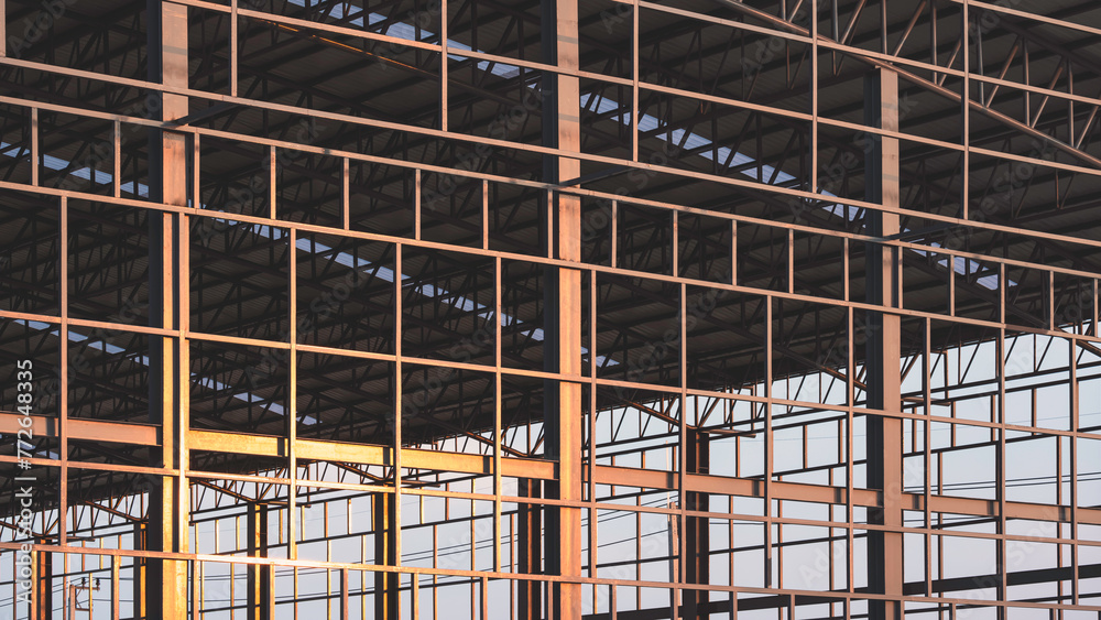 Black metal industrial factory building structure and curve roof outline in construction site with golden sunlight reflection on surface in evening time