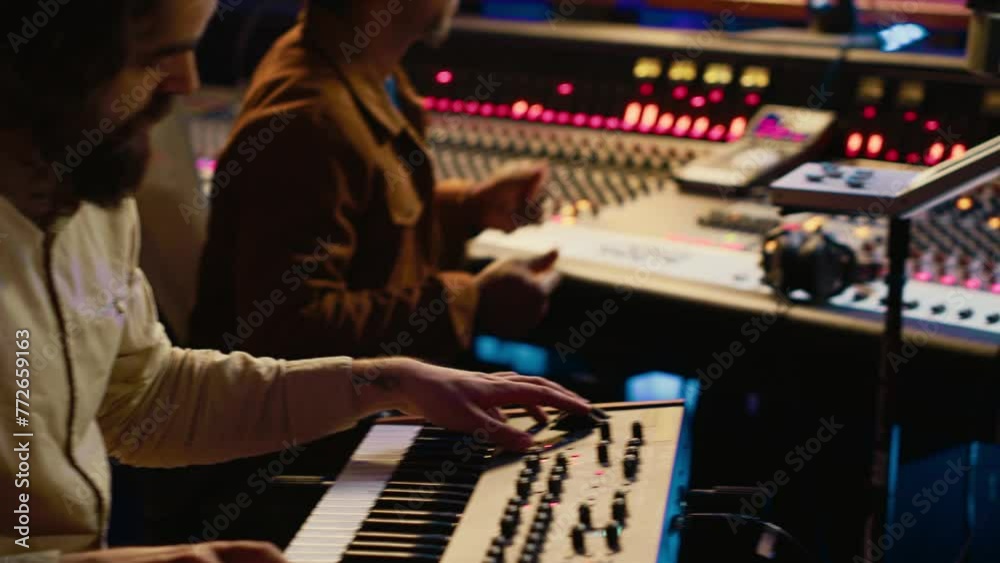 Musician artist playing midi controller synthesizer in recording music studio, composing tracks on mixing console. Singer performing on piano electronic keyboard in control room. Camera A. Musician artist playing midi controller synthesizer in recording music studio, composing tracks on mixing console. Singer performing on piano electronic keyboard in control room. Camera A.
