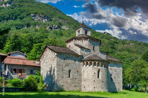 Historical Romanesque Stone Church in European Valley with Bell Tower, Lush Greenery, and Mountainous Backdrop
