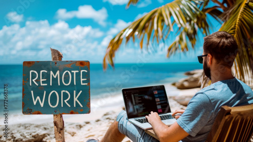 A man is sitting on a beach with remote working laptop in front of him.