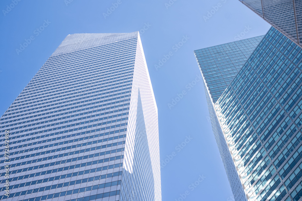 Gaze upwards at the sleek geometry of New York's skyscrapers, where the contrast of glass against the blue sky epitomizes urban aspiration