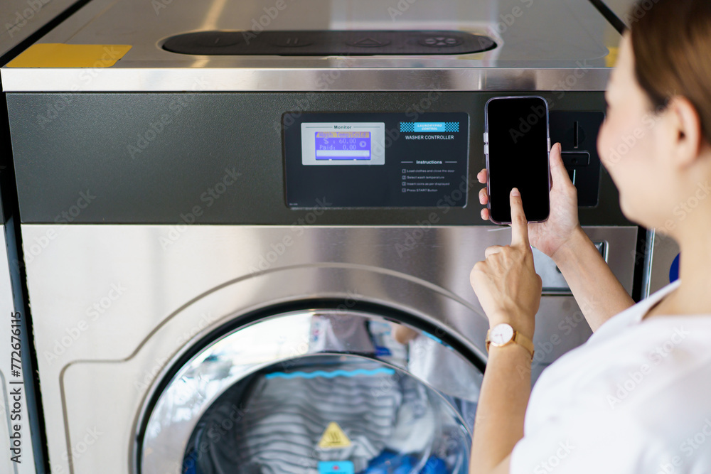 Asian woman using a smartphone payment application to settle for a service cost of using washing machine. Asian woman using a smartphone payment application to settle for a service cost of using washing machine.
