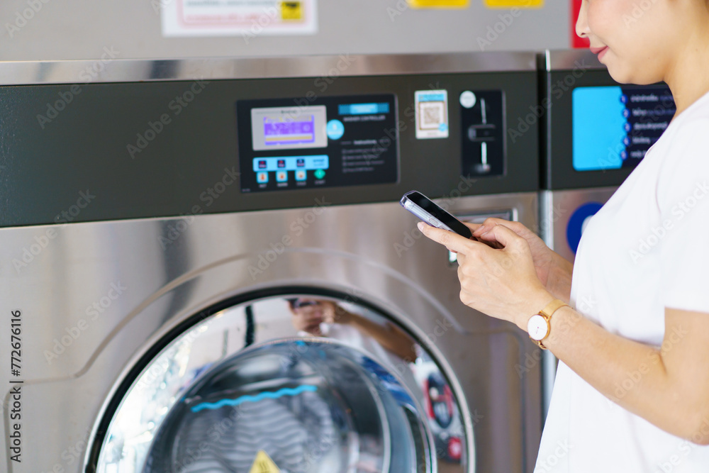 Asian woman using a smartphone payment application to settle for a service cost of using washing machine. Asian woman using a smartphone payment application to settle for a service cost of using washing machine.