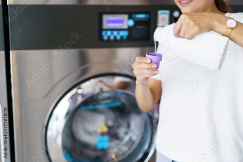 Asian woman pouring liquid detergent into washing machine. 