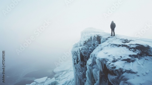 A person stands on the edge of a frozen cliff peering out at the jagged ice formations below. body is silhouetted against the . .