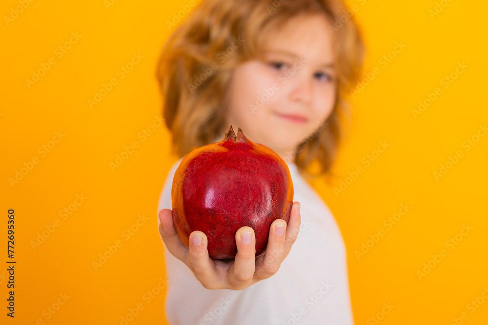 Kids face with fruits. Kid hold red pomegranate in studio. Pomegranate fruit. Studio portrait of cute child with pomegranate isolated on yellow background. Kids face with fruits. Kid hold red pomegranate in studio. Pomegranate fruit. Studio portrait of cute child with pomegranate isolated on yellow background.
