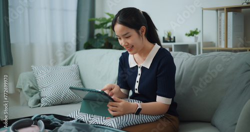 Portrait of Asian teenager woman sitting on sofa planning vacation trip and searching information on digital tablet, travel and lifestyle. © Johnstocker
