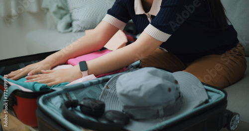 Selective focus hands of Asian teenager woman sitting on sofa packing travel luggage with clothes for traveling trip, Preparation travel suitcase at home. © Johnstocker