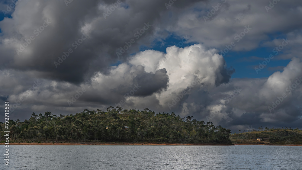 A dense forest grows on the hilly shores of a calm lake. Ripples on the water. Picturesque cumulus clouds in the blue sky.Madagascar. Mantasoa Lake