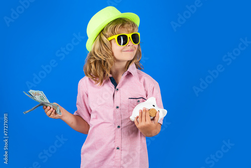 Dollars money and piggybank concept. Portrait of a little boy putting money on a moneybox. Child saving money in a piggybank on blue background.