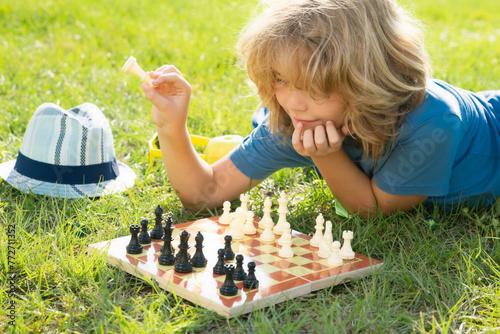 Kid thinking of chess. Clever concentrated and thinking child playing chess outdoor in park.