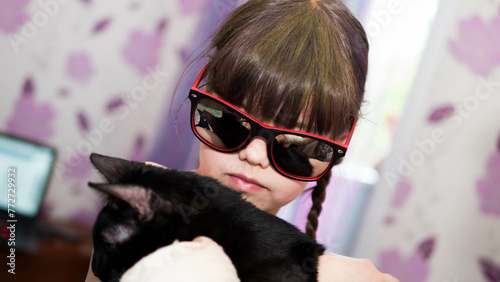 little girl in sunglasses holding a black cat in her arms (ID: 772729932)