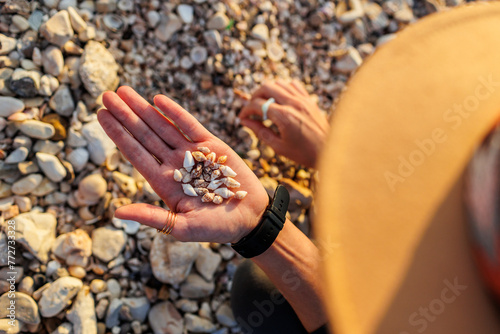 Foto young girl in a hat sits on the beach and collects various shells